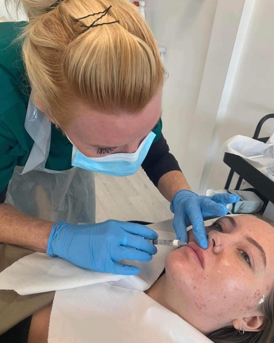 Rachel, gloved and masked, treating a client's lips in her treatment room